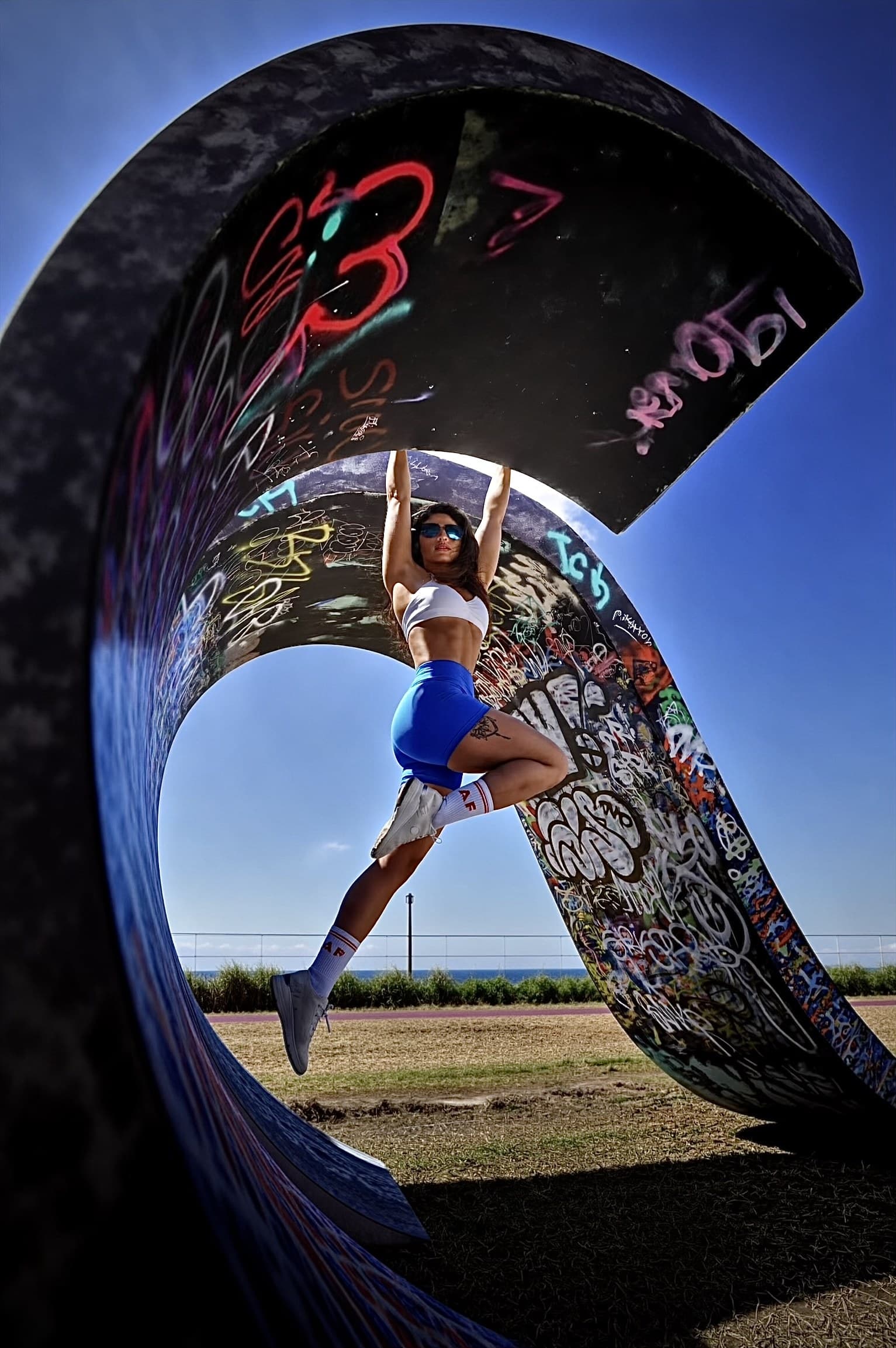 Lara Rojas suspendue à une arche de béton couverte de graffitis, face à la mer